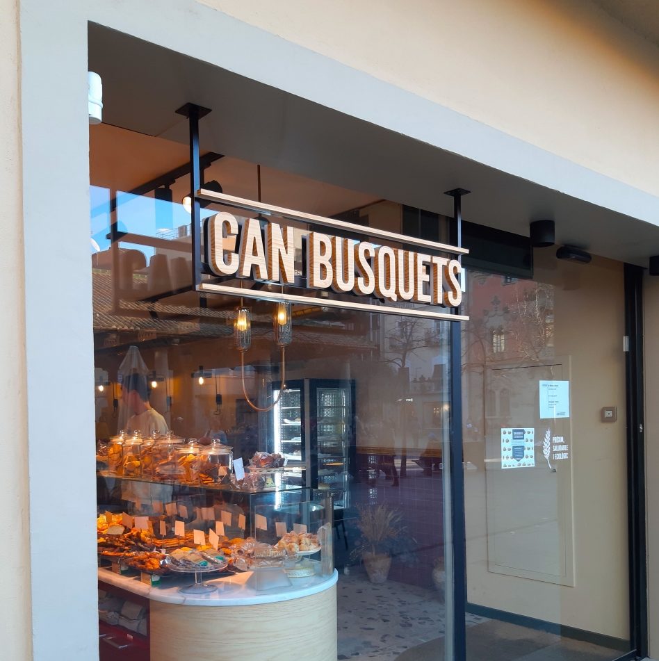 Enseigne Can Busquets avec lettres lumineuses suspendues en intérieur derrière vitrine