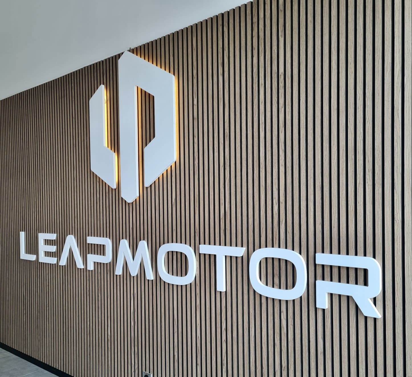 Enseigne et lettres rétro-éclairées LEAPMOTOR sur mur en tasseaux bois verticaux à Toulouse