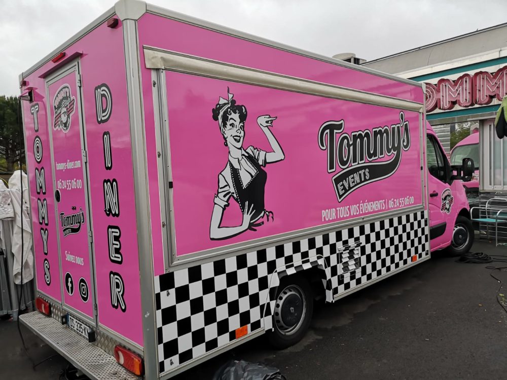 Véhicule rose floqué Tommy’s Events avec logo rétro, coordonnées et visuel diner américain
